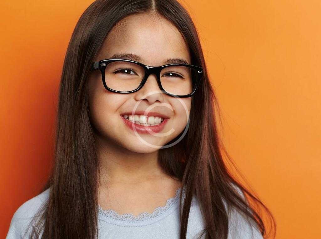 Smiling girl wearing glasses with an orange background.