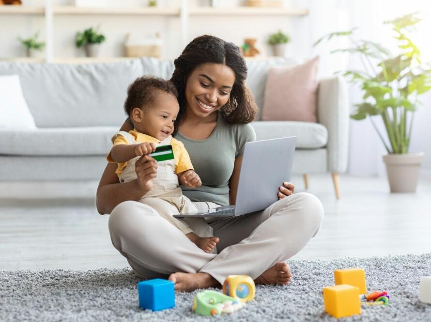 Black Mother With Infant Baby Using Laptop For Online Shopping At Home