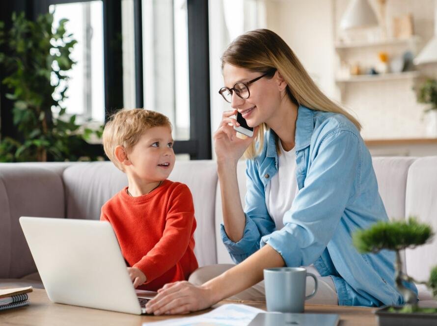 Busy working remotely mother taking care of her little toddler baby son kid child on freelance