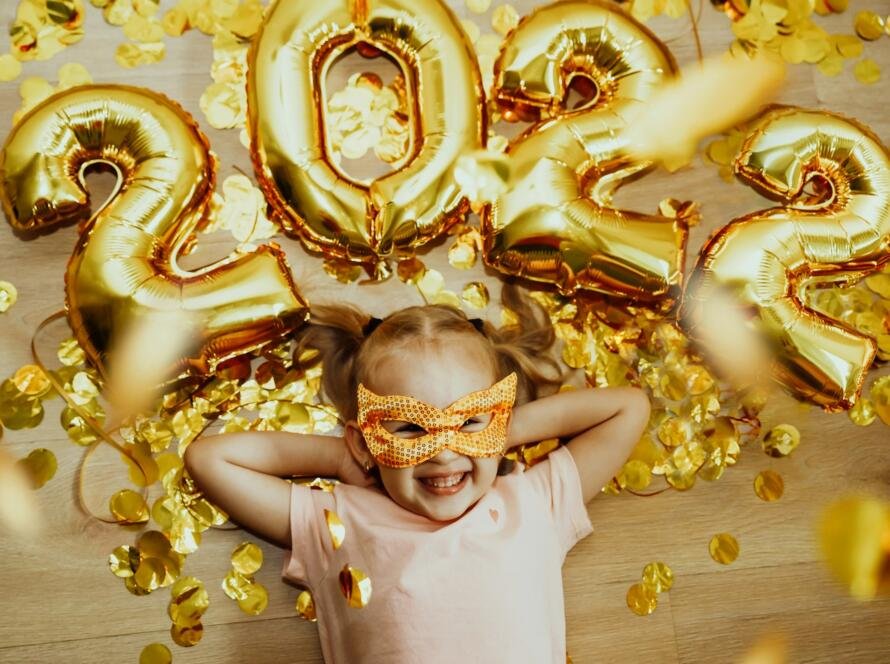 Cheerful Baby girl in mask with numbers 2022 rejoices at the confetti flying from above