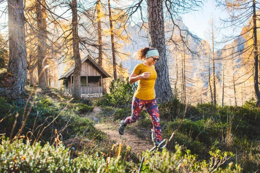 Cheerful caucasian woman on a hike running trough the autumn forest, sun rays shining trough the