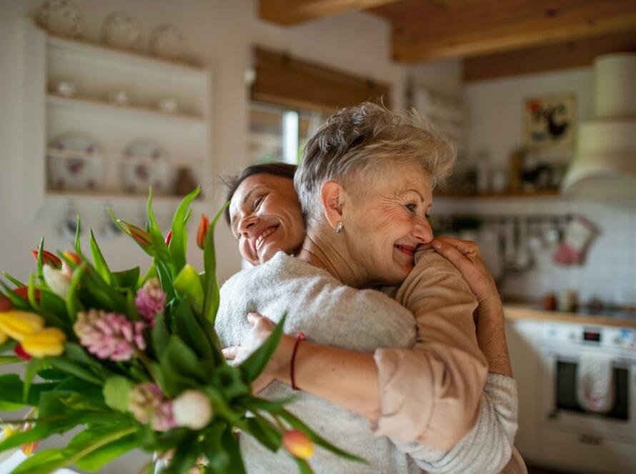 Happy senior mother hugging adult daughter indoors at home, mothers day or birthday celebration