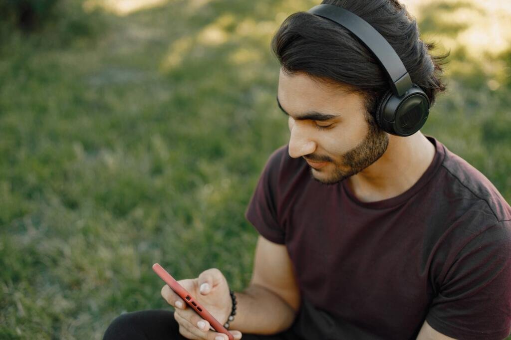 Male indian student sitting on a grass and using a smatphone