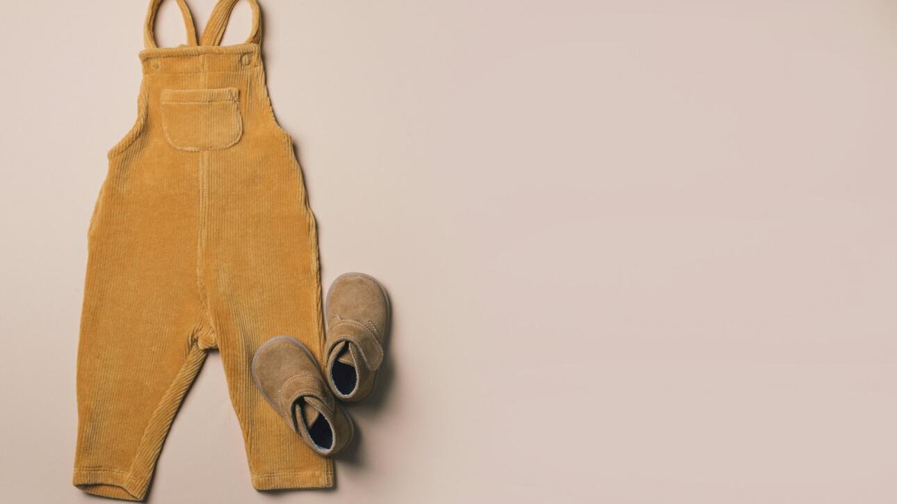 Mustard baby romper, shoes, yellow autumn leaves on beige background. Set of baby clothes