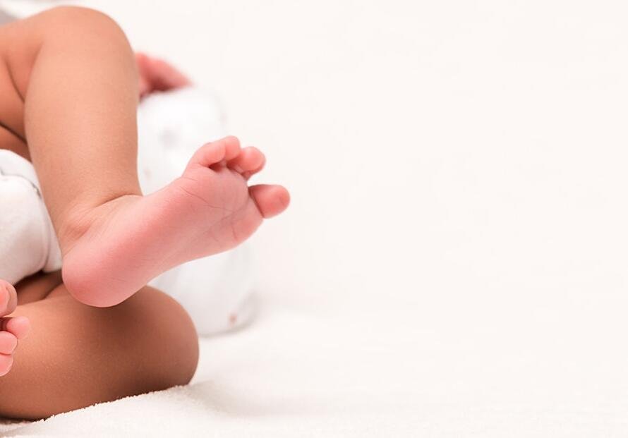 panoramic shot of newborn in baby romper lying on white