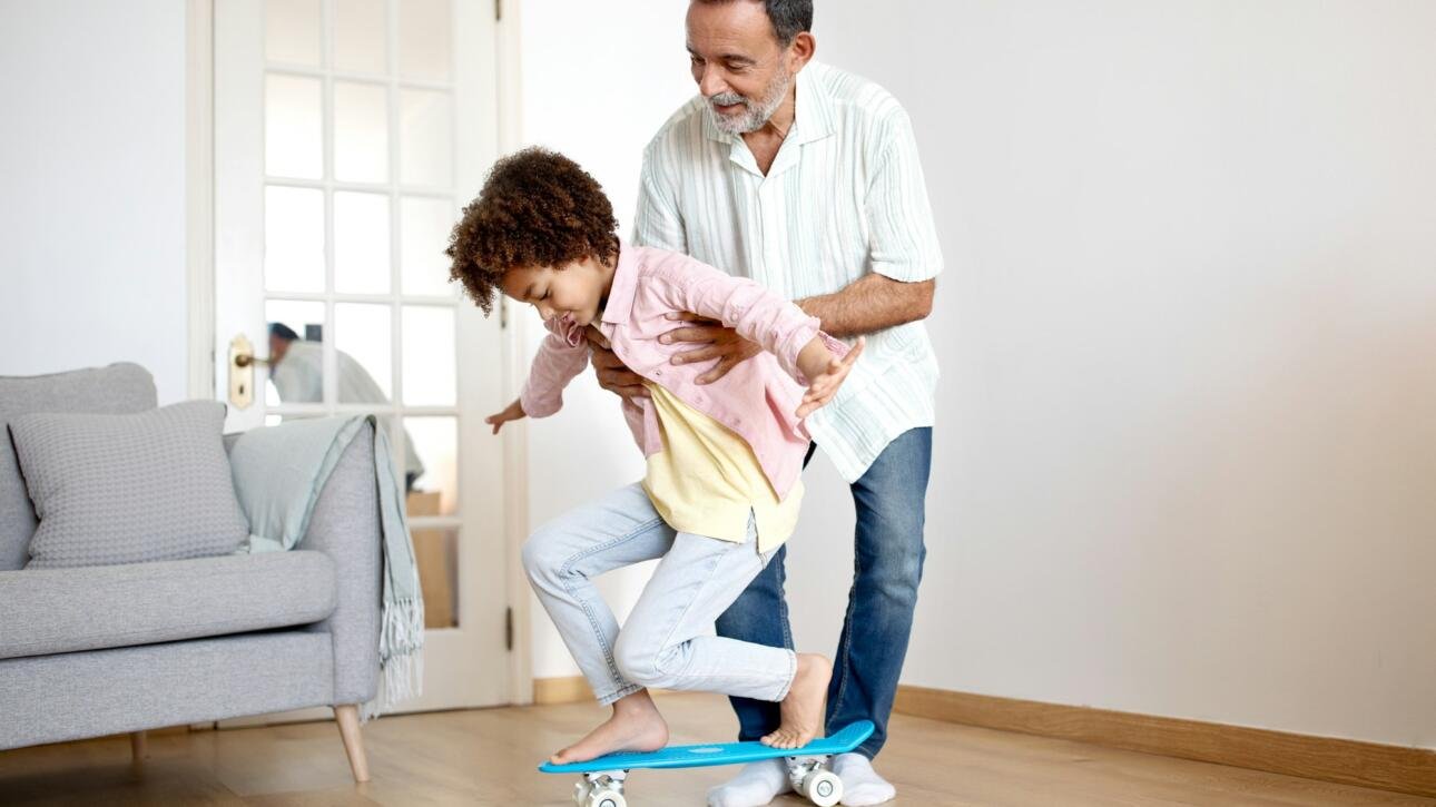 Smiling Latin Grandfather Guides Grandson's First Skateboard Ride at Home