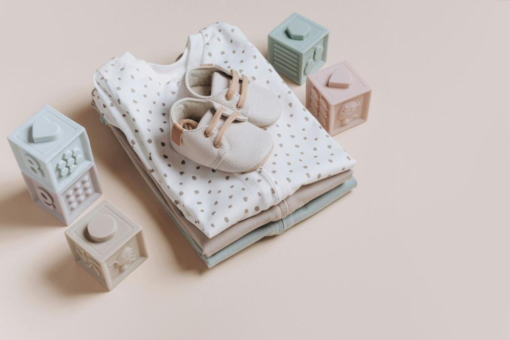 Stack of organic cotton bodysuits, rompers, baby shoes and silicone toys, pyramid