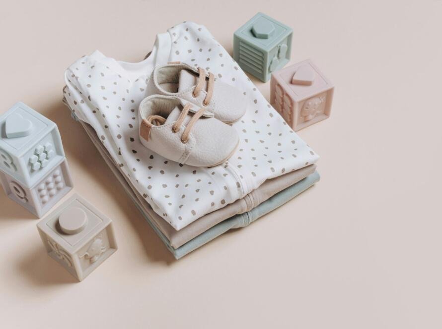 Stack of organic cotton bodysuits, rompers, baby shoes and silicone toys, pyramid