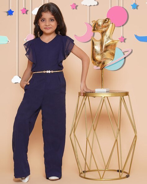 A young girl in a navy blue jumpsuit stands next to a modern golden table, against a whimsical backdrop with stars, clouds, and planets.