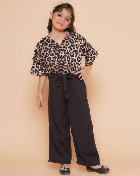 Young girl wearing a leopard print top and black wide-leg trousers, standing against a beige background.