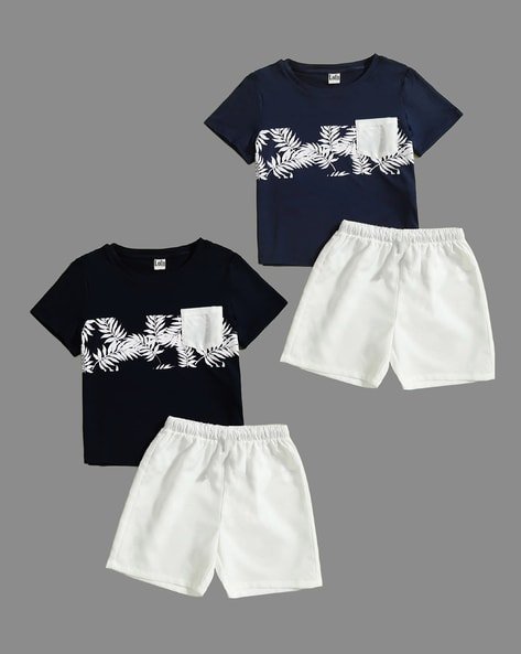 Two matching children's outfits consisting of a navy blue T-shirt with a white leaf pattern and a white pocket, paired with white shorts.