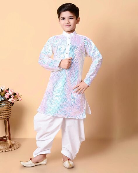 Boy wearing a white sequined traditional kurta with white pants and mojaris, standing against a beige background.