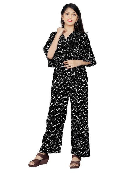 A woman wearing a black polka dot jumpsuit with wide-legged pants and wedge sandals.