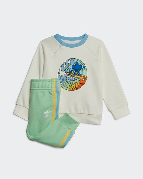 Children's Adidas tracksuit with a white sweatshirt featuring a colourful circular graphic design and light green trousers with multicoloured stripes on the side.